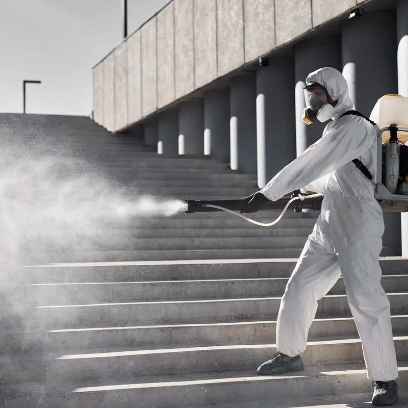 Technicien en tenue de protection pulvérisant un traitement dans un escalier